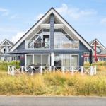 Modernes Ferienhaus mit Balkon und Terrasse. Umgeben von Gras und Nachbarhäusern.