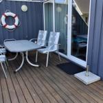 Terrasse mit Tisch und Stühlen, Rettungsring an Wand, Holzdecke und Glastür.