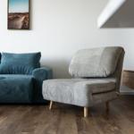 Ein Raum mit blauem Sofa und grauem Sessel auf Holzboden.