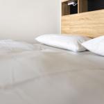 Doppelbett mit weißer Bettwäsche und Holzkopfteil.