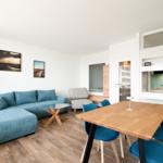 Wohn- und Essbereich mit blauem Sofa, Holztisch und Küchenbereich.