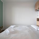 Schlafzimmer mit Bett, weißen Laken und Holzschränken an der Wand.