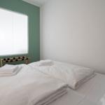 Schlafzimmer mit weißem Bett, grüner Wand und Fenster mit Jalousie.