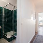 Badezimmer mit Dusche und Toilette. Flur führt zum Balkon.