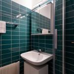 Badezimmer mit grünen Fliesen, Waschbecken, Spiegel und Dusche.