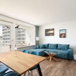 Wohnung mit Essbereich, Sofa und Balkon. Blick auf Gebäude und Himmel.