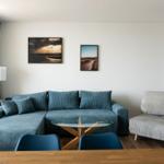 Wohnzimmer mit blauem Sofa, Glas-Tisch und Wandbildern.