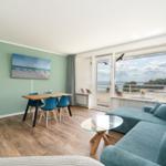Wohnzimmer mit Sofa, Esstisch und Balkonblick auf Wasser