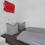 Schlafzimmer mit Bett, Kissen und Wandbild. Nachttisch mit Lampe daneben.