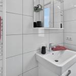 Badezimmer mit weißer Fliesenwand, Waschbecken, Spiegel und Handtuchhalter.