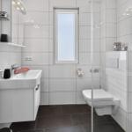 Badezimmer mit Dusche, Toilette und Waschbecken. Weiße Fliesen und dunkle Bodenfliesen.