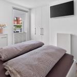 Schlafzimmer mit Bett, Kleiderschrank und TV. Fenster mit Blick auf Gebäude.