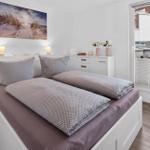 Schlafzimmer mit Doppelbett, weißen Möbeln und Blick auf Balkon.