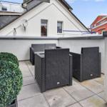 Terrasse mit Gartenmöbeln und Topfpflanze. Blick auf benachbarte Gebäude.