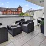 Terrasse mit Sitzgruppe und Blick auf ein rotes Gebäude.