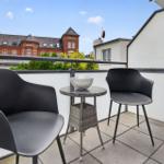 Terrasse mit zwei Stühlen und Tisch. Im Hintergrund ein rotes Gebäude.