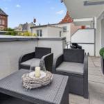 Terrasse mit zwei Sesseln, Tisch und Pflanzen. Blick auf umliegende Gebäude.