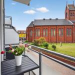 Balkon mit Blumen und Blick auf eine rote Backstein-Kirche mit Grünfläche.