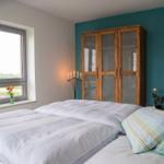 Schlafzimmer mit Bett, Kleiderschrank und Sofa. Fenster mit Blick auf Feld.