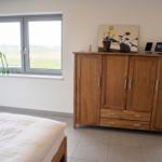Zimmer mit Bett, Tisch, Stuhl und Bücherregal. Fenster mit Blick auf Feld.