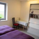 Schlafzimmer mit Bett, Nachttisch und Fenster. Blick auf Felder.