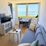 Wohnzimmer mit Sofa, Esstisch und TV. Blick auf Hafen und Meer.