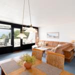 Wohn- und Essbereich mit Blick aufs Meer und Terrasse. Holztisch, Sofa und Wandbilder.