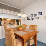 Essbereich mit Holztisch, Stühlen und Küchenbereich im Hintergrund.