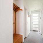 Flur mit Holzgarderobe, Tür und Fenster. Teppichboden und weiße Wände.