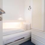 Schlafzimmer mit weißem Bett, Kleiderschrank und Ankerdekoration an der Wand.