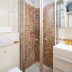 Bad mit Dusche, Waschbecken und Toilette. Fliesenwand und Spiegel sichtbar.