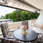 Terrasse mit Tisch, Stühlen und Blick auf Wasser und Bäume.