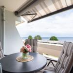 Balkon mit Tisch, Stühlen und Meerblick unter Markise.