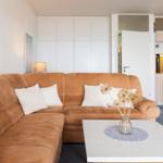 Wohnzimmer mit braunem Sofa, weißem Tisch und Küchenbereich im Hintergrund.