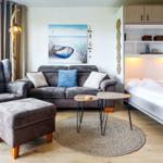 Wohnbereich mit Sofa, Sessel und Bett. Wandbild und Holzmöbel.
