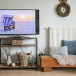 TV auf Ständer mit Körben und Kissen, daneben Holzbank mit Decke.