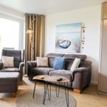 Wohnzimmer mit Sofa, Sessel, Tisch und Wandbild. Holzfußboden und große Fenster.