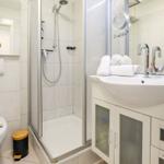 Badezimmer mit Dusche, Waschbecken und Toilette. Weiße Fliesen und moderne Einrichtung.