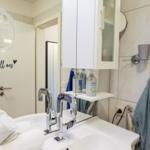 Badezimmer mit Waschbecken, Spiegel, Handtuchhaltern und Duschbereich.