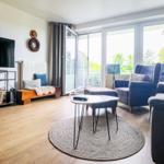 Wohnzimmer mit TV, Sitzgelegenheiten und Blick auf Balkon.