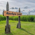 Holzschild mit der Aufschrift Naturhafen Loddin inmitten von Gras und Himmel.