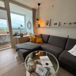 Ein Wohnzimmer mit grauem Sofa, Glas-Tisch und Blick auf Balkon.
