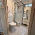 Badezimmer mit Dusche, Waschbecken und Toilette. Fliesenboden und Wandverkleidung.