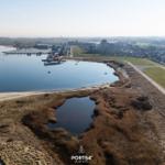 Aerial view of a waterfront with docks, residential buildings, and natural wetlands.