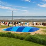 Strand mit bunten Strandkörben und blauem Springbecken. Menschen spielen und entspannen.