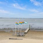 Strand mit Flaggen, Steg und Statue am Wasser.