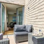 Terrasse mit Sitzgruppe und Tisch. Durchgehende Glastüren führen ins Wohnzimmer.