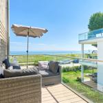 Terrasse mit Sitzgruppe und Sonnenschirm. Blick auf das Meer und grünen Garten.