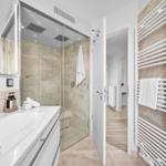Bad mit Dusche, Waschbecken und Heizkörper. Tür führt in das Zimmer.