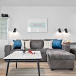 Wohnzimmer mit grauem Sofa, Tisch und Küchenbereich.